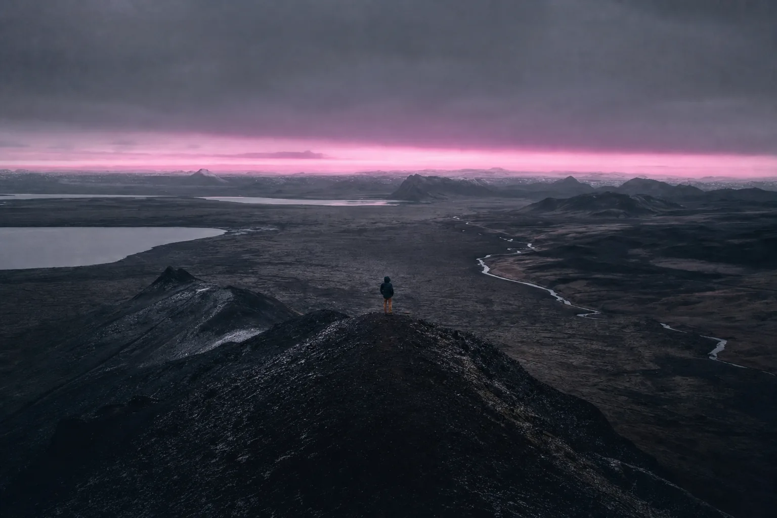 Crête volcanique islandaise au crépuscule, une bande de lumière rasante souligne l'horizon, une silhouette se tient sur l'arête.
